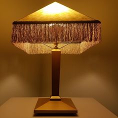 a lamp that is sitting on top of a white table with a brown base and fringed lampshade