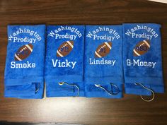 three blue towels with embroidered footballs on them sitting on a wooden table next to a pair of fishing hooks