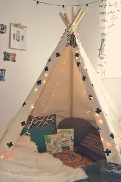 a teepee tent with lights and pillows on the floor in front of some pictures