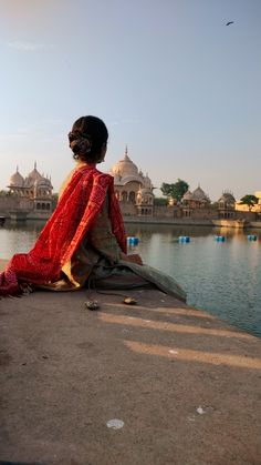 a woman sitting on the edge of a pier looking out over water with buildings in the background