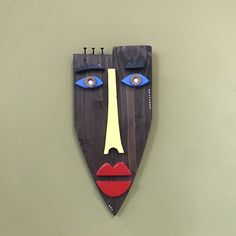 a wooden mask hanging on the wall with blue eyes and red lipstick painted on it