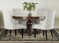 a dining room table with white chairs and a vase filled with flowers on top of it