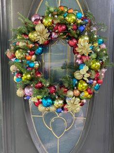 a christmas wreath on the front door of a house with ornaments hanging from it's sides