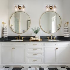 two round mirrors are above the double sinks in this white bathroom with black and gold accents