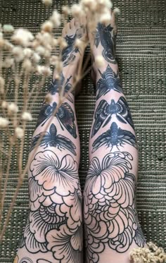 a woman's legs with tattoos on them and flowers in front of her feet