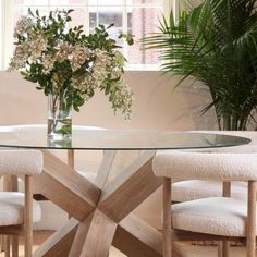 a glass table with chairs around it and flowers in a vase on the table top