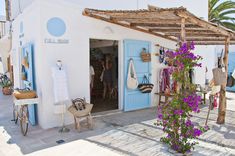 a white building with blue doors and purple flowers on the outside, next to an open door