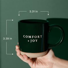 a hand holding a black coffee mug with the words comfort and joy printed on it