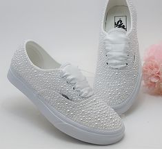 a pair of white tennis shoes next to a pink flower on a white tablecloth