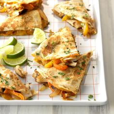 several quesadillas on a white plate with limes and sliced cucumbers