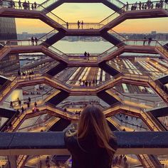 a woman standing on top of a building looking down at the street below her is an escalator with people walking up and down it