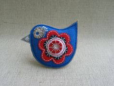 a small blue bird with a red flower on it's head and two buttons in the center