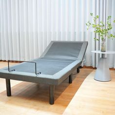 a bed sitting on top of a hard wood floor next to a white table with a potted plant