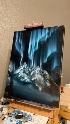 an artist's easel with a painting on it that has the aurora lights in the sky