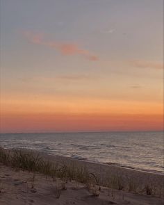 a bench sitting on top of a sandy beach next to the ocean at sunset or dawn