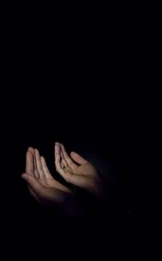 two hands reaching up in the dark to touch each other with their palms on top of one another