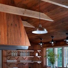 a kitchen with wooden walls and ceilinging has wine glasses on the shelves, along with hanging lights