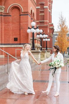 a bride and groom holding hands in front of an old brick building on a rainy day