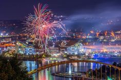 fireworks are lit up in the night sky over a river and cityscape with buildings