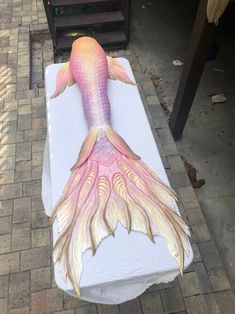 a large pink and white fish sculpture sitting on top of a table next to a brick walkway