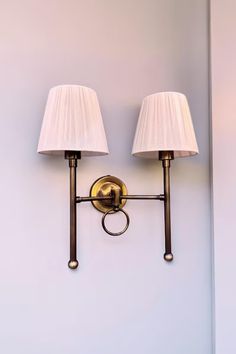 two lamps mounted on the wall next to each other with white shades and gold trim