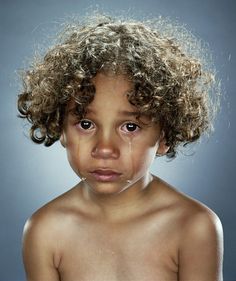 a young child with curly hair has tears on his face and is frowning at the camera