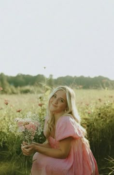 a woman in a pink dress sitting on the ground with flowers and grass behind her