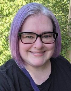 a woman with purple hair and glasses smiling