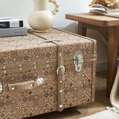 an old suitcase sitting on the floor next to a table with a vase and books