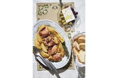 a plate with meat and potatoes on it next to bread, olives and butter