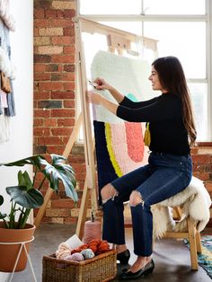 a woman sitting on a chair in front of an easel