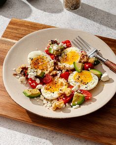 a white plate topped with eggs and vegetables on top of a wooden cutting board next to a fork