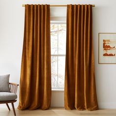 an orange curtain hanging in front of a window with a chair and painting on the wall