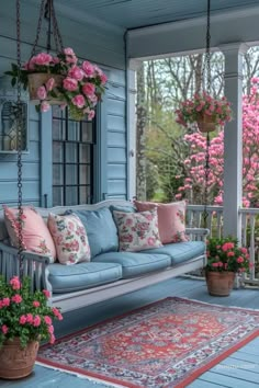 a blue porch with pink flowers and hanging planters on the porch swings down onto an area rug