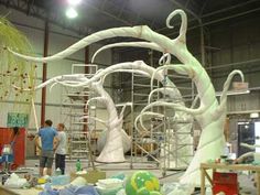 two men working on an art piece in a large room with scaffolding and balloons