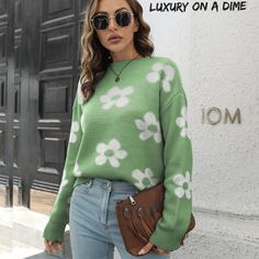 a woman standing in front of a building wearing a green sweater with white flowers on it