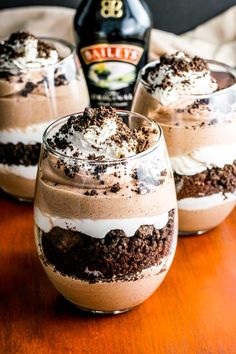 three glasses filled with dessert sitting on top of a wooden table