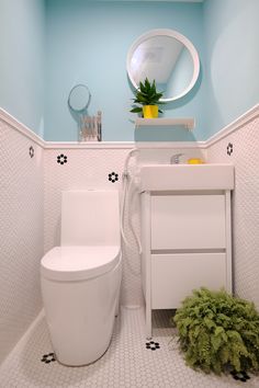 a white toilet sitting next to a sink in a bathroom under a mirror and potted plant