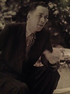 an old photo of a man in a suit and tie sitting on a stone bench