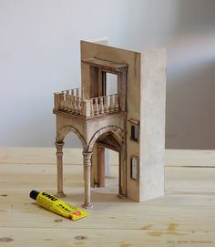 a doll house with a staircase and balcony next to a yellow marker on a wooden table