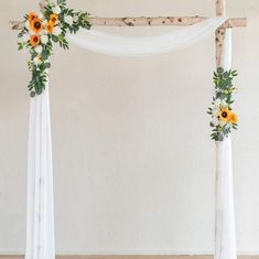 an arch decorated with sunflowers, greenery and white drapes for a wedding ceremony