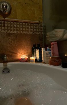 a bathtub filled with lots of soap next to a candle and some other items