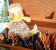 a wooden box filled with lots of colorful crayons and a doll in it