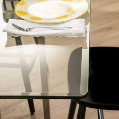 there is a glass table with plates and silverware on it, next to a black chair