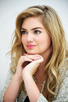 a woman with long blonde hair and blue eyes posing for a photo in front of a white wall