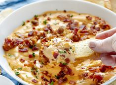 a hand dipping a piece of bread into a bowl of cheesy potato soup