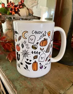 a white coffee mug with candy and pumpkins painted on it sitting on a table