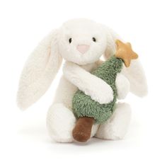 a white stuffed rabbit holding a green christmas tree ornament in its paws, with a gold star on it's chest