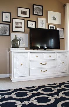 a white entertainment center with pictures on the wall and an area rug in front of it