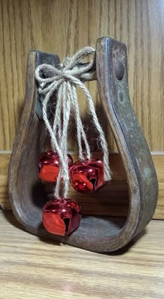 some red glass bells are hanging from a wooden holder with twine strings attached to them